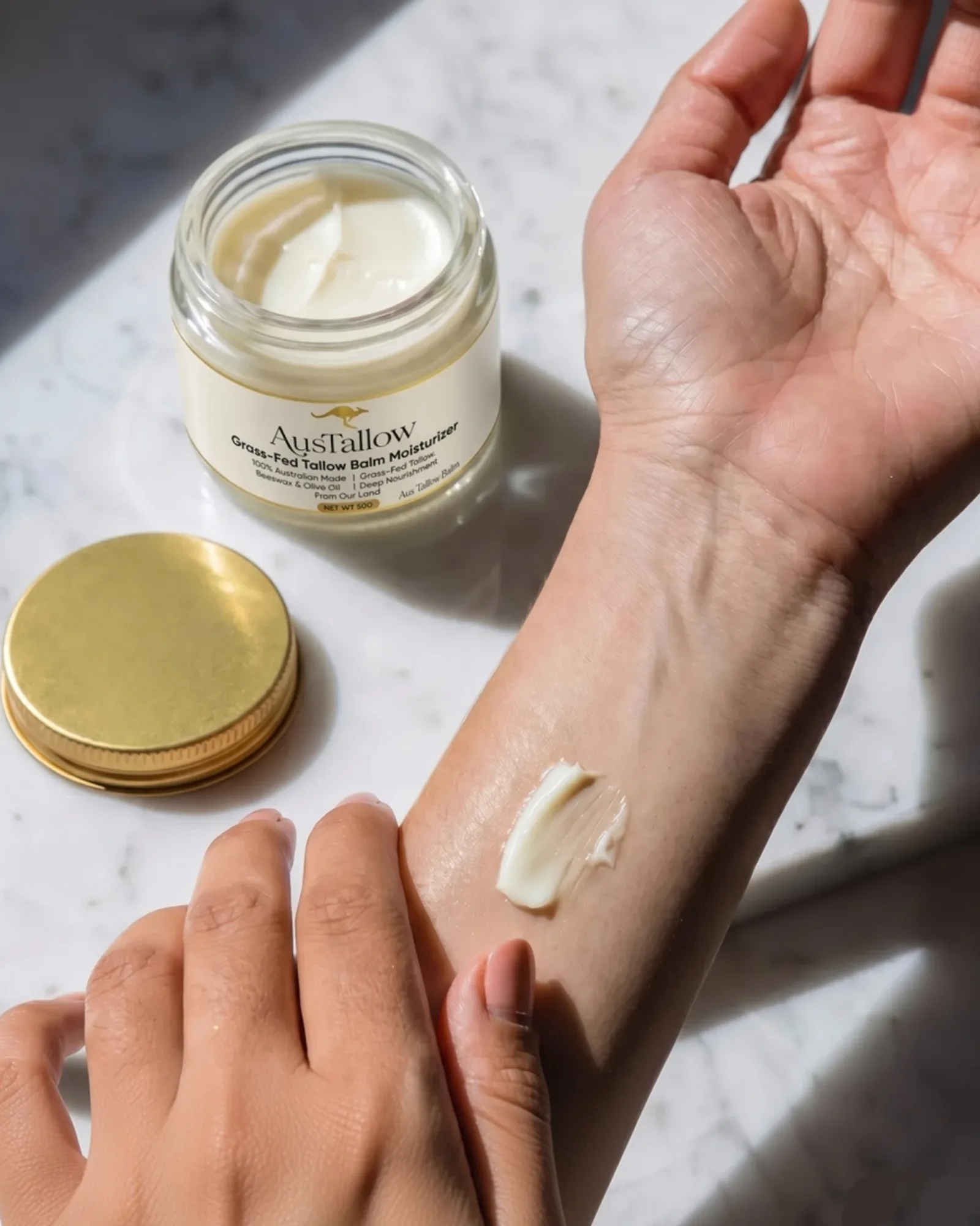 A swatch of AusTallow balm on a forearm beside the open jar on marble